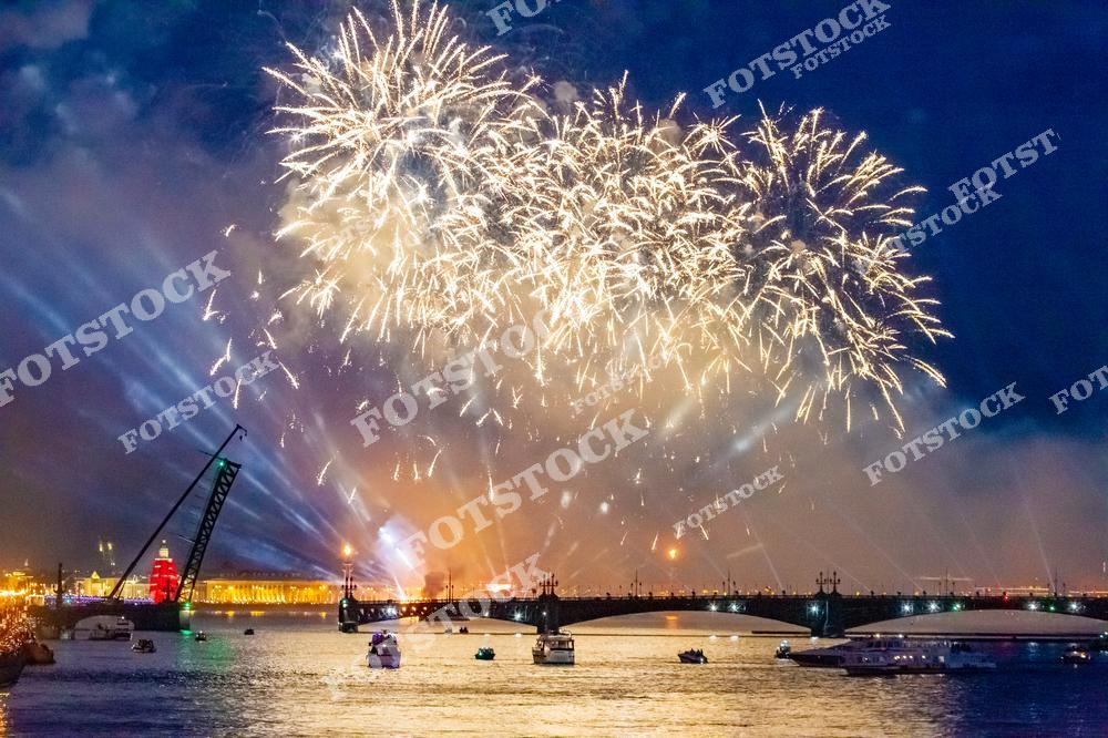 На фотографии запечатлен яркий фейерверк, освещающий ночное небо Санкт-Петербурга. На фоне виден Троицкий мост, соединяющий берега Невы, и разведение его створок добавляет драматичности композиции. Река Нева отражает огни, усиливая красоту зрелища. Эта сцена передает торжественную атмосферу белых ночей и праздничных мероприятий города.